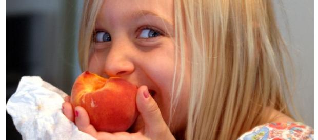 Young kid eating an apricot and smiling. Young kid eating an apricot and smiling.
