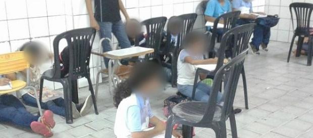 Sem carteiras, alunos assistem aula no chão Sem carteiras, alunos assistem aula no chão