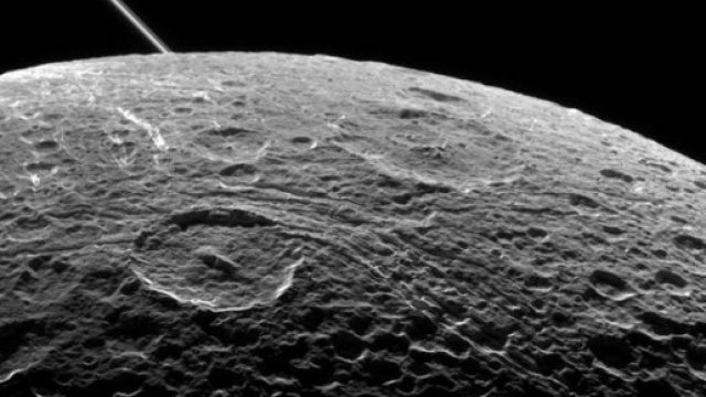 Dione, ripresa effettuata da Cassini durante l'ultimo fly-by (sorvolo ravvicinato) del16 giugno 2015. Sullo sfondo la linea degli anelli di Saturno