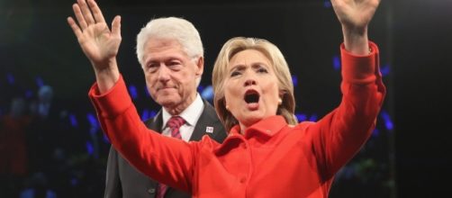 Hilary Clinton vestita di rosso con alle spalle il marito Bill, al primo dibattito con Trump