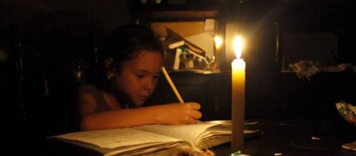 Una bambina scrive a lume di candela