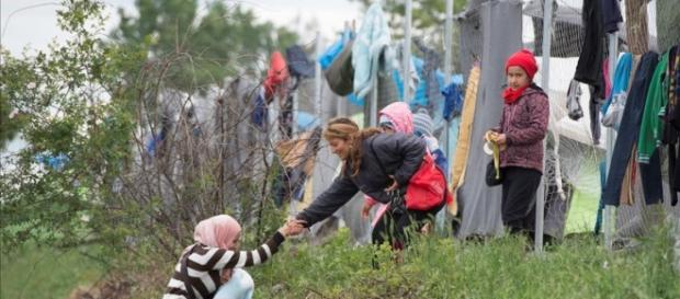 Una refugiada con un bebé en brazos es ayudada por otra refugiada Una refugiada con un bebé en brazos es ayudada por otra refugiada
