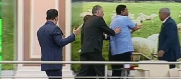 Na imagem o momento em que o pastor sai do palco já tampando com a mão um dos lugares do ferimento. Na imagem o momento em que o pastor sai do palco já tampando com a mão um dos lugares do ferimento.