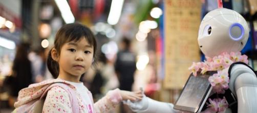 Una bambina porge la mano a un robot tra le vie del mercato di Osaka