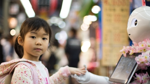 Una bambina porge la mano a un robot tra le vie del mercato di Osaka