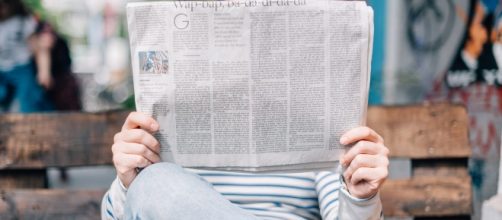 Un giovane legge un quotidiano seduto su una panchina per le strade di Berlino