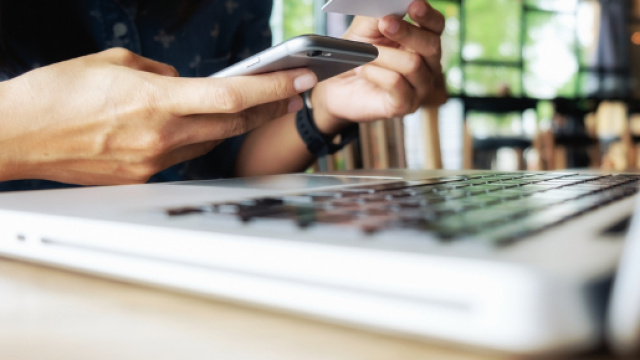 Una persona davanti al computer con il cellulare in mano