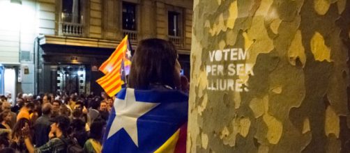 Women dressed in the Catalan independence flag stands next to a spray painted tree that reads in Catalan "We vote for being free"