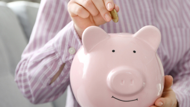 Un salvadanaio rosa e una donna che mette una moneta da 50 centesimi