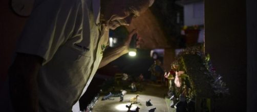 A man shines a torch over a nativity scene in Puerto Rico. Photo Credit: The Chicago. Tribune