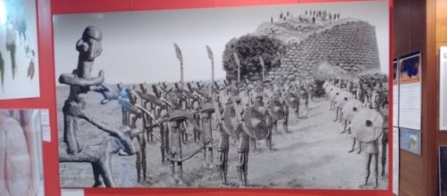 Foto della mostra Omphalos raffigurante un nuraghe e un esercito di bronzetti nuragici.