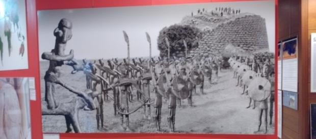 Foto della mostra Omphalos raffigurante un nuraghe e un esercito di bronzetti nuragici. Foto della mostra Omphalos raffigurante un nuraghe e un esercito di bronzetti nuragici.