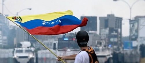 Protester waving venezuelan flag credits:wikimedia https://upload.wikimedia.org/wikipedia/commons/3/30/2017_Venezuelan_protests_flag.jpg