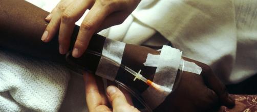 Two hands manipulating an IV for chemotherapy administration. [image via National Cancer Institute, Wikimedia Commons]