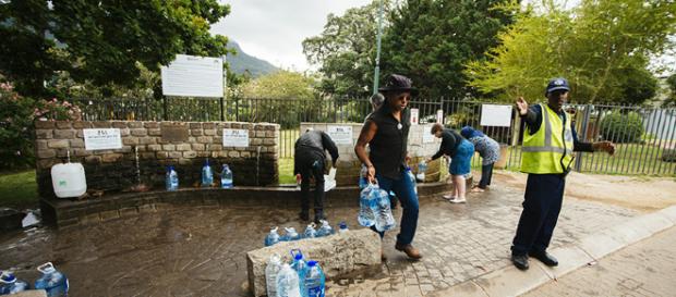 Un oficial de seguridad dirige a los residentes mientras llenan botellas de agua en el manantial natural de Newlands en Ciudad del Cabo Un oficial de seguridad dirige a los residentes mientras llenan botellas de agua en el manantial natural de Newlands en Ciudad del Cabo
