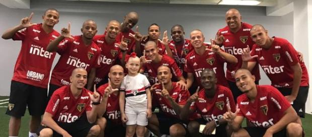 Pequena torcedora ao lado dos jogadores (Divulgação SPFC). Pequena torcedora ao lado dos jogadores (Divulgação SPFC).