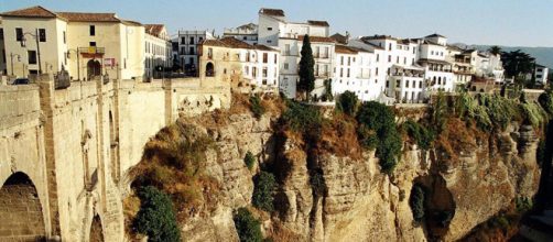 Houses cling to the cliffs alongside the New Bridge and the El Tajo Gorge in Ronda, Spain. [Image TUI/Wikimedia]