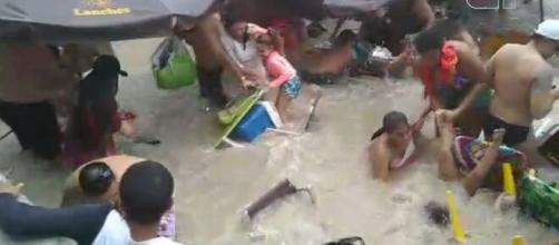 Banhistas tentam salvar pertences em meio à água que invadiu a areia. (Reprodução/Redes Sociais)