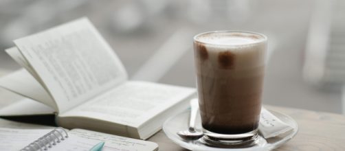 Libro con penna e cappuccinosu scrivania- © Pexels