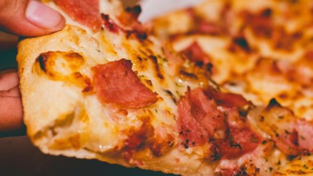Una fetta di pizza che viene sollevata © Pexels