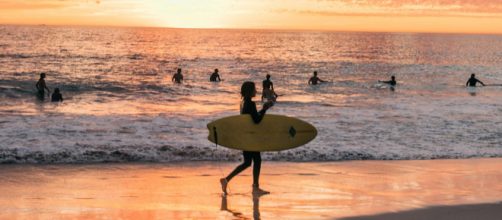 Donna con tavola da surf al mare - © Pexels