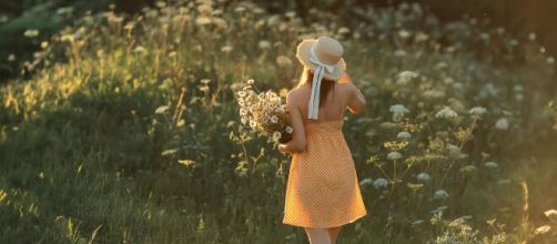 Ragazza di spalle con in mano dei fiori © Pexels