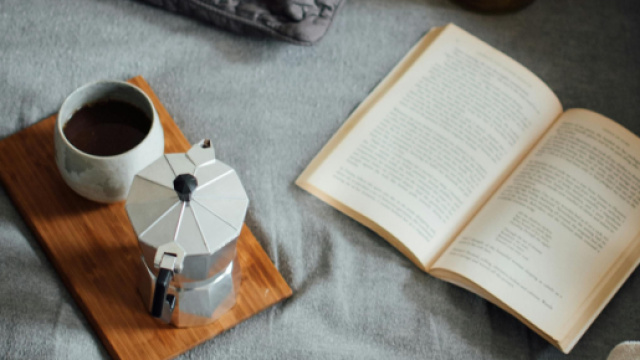 Tazza di caffé con caffettiera e llbro aperto sul letto- © Pexels
