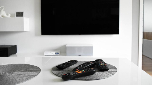 Salotto moderno con tv a parete e quattro telecomandi sul tavolo © Pixabay.