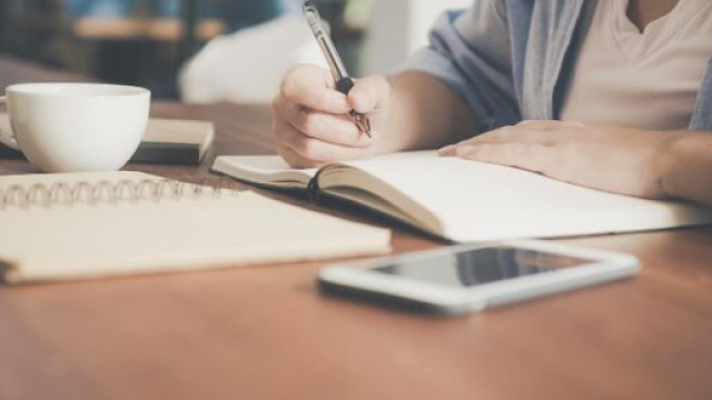 Una figura intenta a scrivere su un quaderno - © Pexels