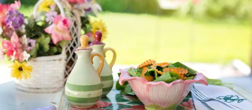 Tavolo all’aperto con centrotavola floreale, olio, aceto e insalata fresca – © Pixabay.