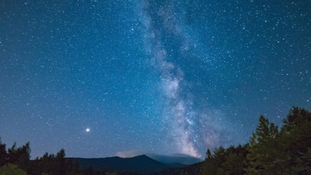 Galassie nel cielo stellato, alberi e monti © Pexels.com