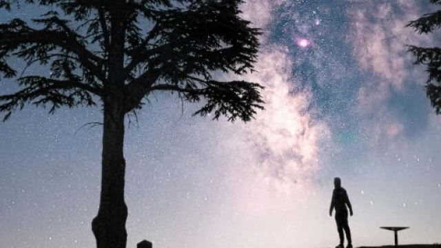 Una persona in silhouette osserva la Via Lattea in un paesaggio notturno – © Pexels.